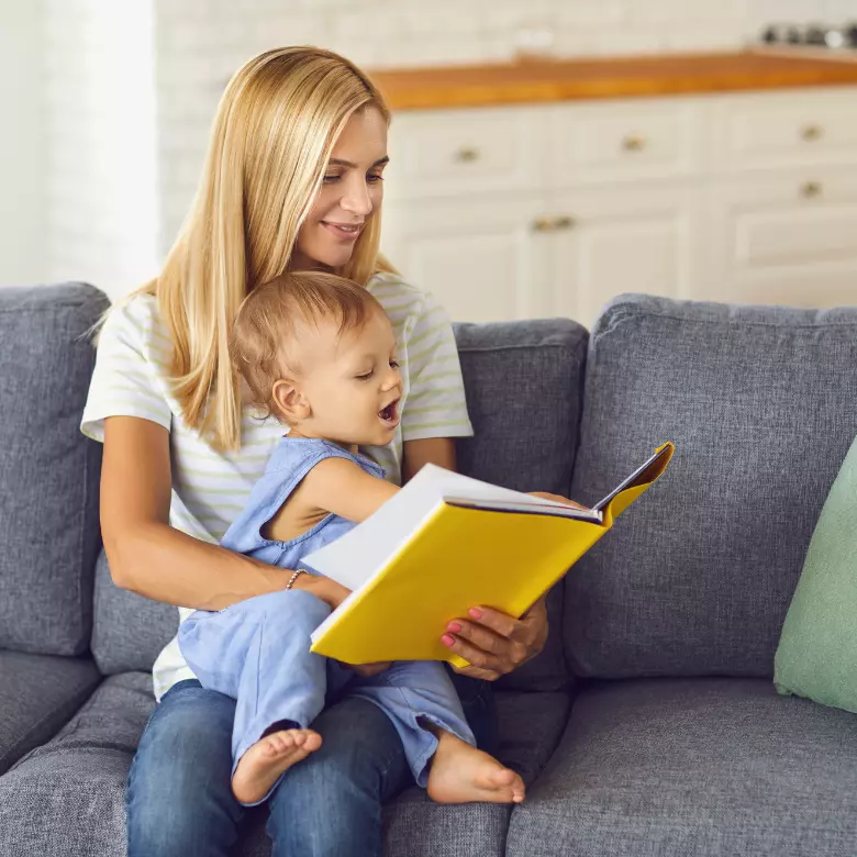 Babá sentada no sofá lendo um livro para um bebê