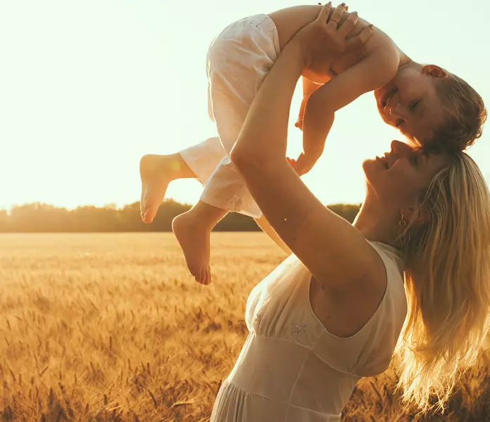 Uma mãe feliz segurando o filho e encostando sua cabeça na dele, em meio a um campo