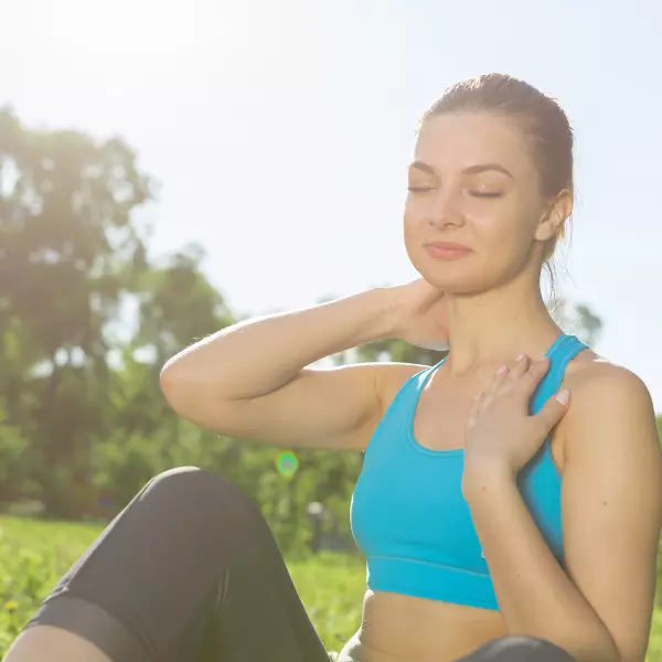 Mulher com trajes esportivos sentada na grama e tomando sol.
